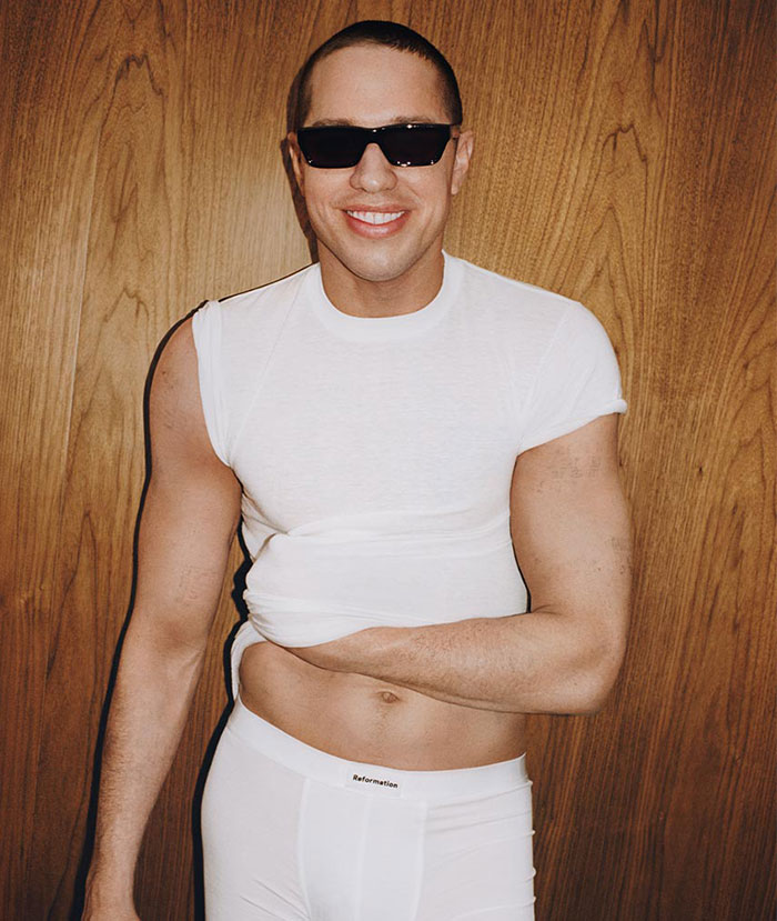 Pete Davidson posing in Reformation apparel, wearing sunglasses and a white outfit, related to tattoo removal.