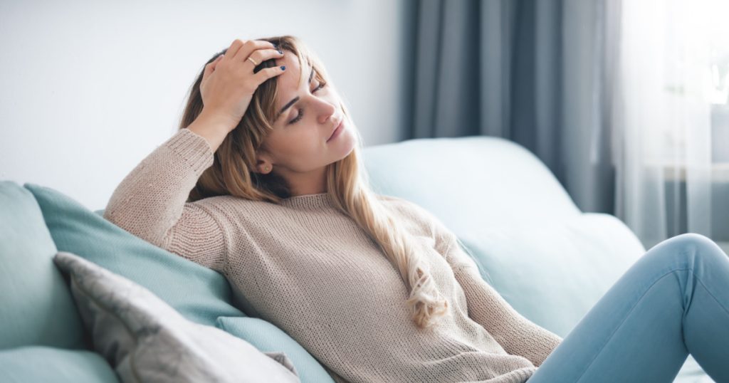 Sad woman sitting on sofa at home, thinking about important things
