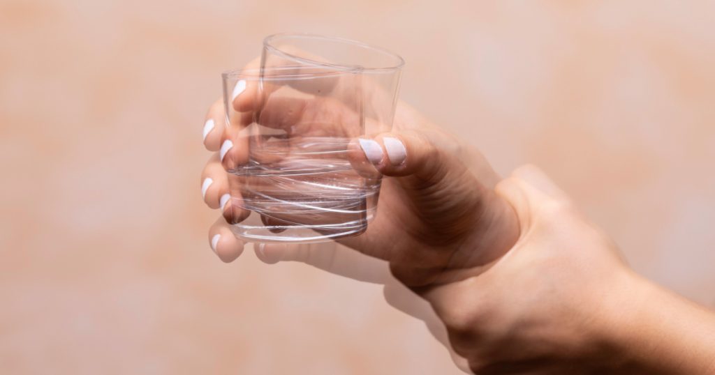 Closeup view on the shaking hand of a person holding drinking glass suffering from Parkinson's disease
