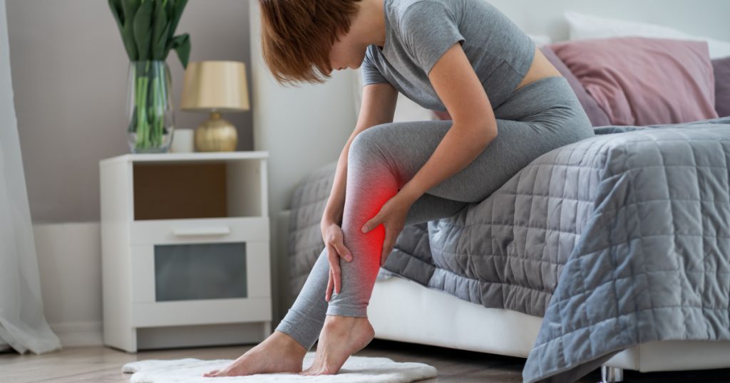 woman's calf muscle cramped, massage of female leg in home interior, painful area highlighted in red