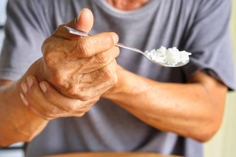 Elderly man is holding his hand while eating because Parkinson's disease.Tremor is most symptom and make a trouble for doing activities such as eat.Health care or elderly concept.Selective focus.
