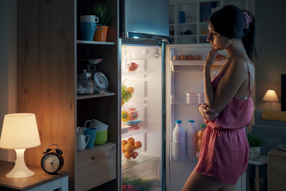 Young woman looking in the fridge at night, she is hungry
