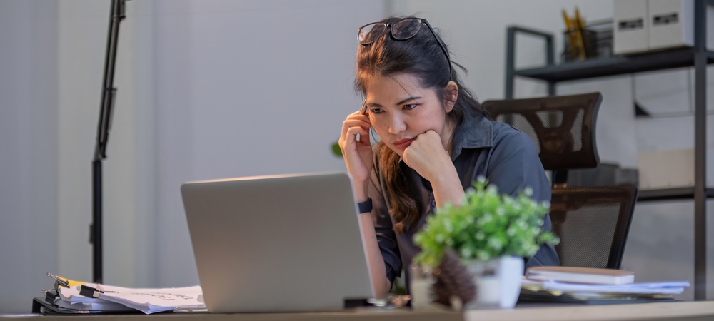 Puzzled confused asian woman thinking hard concerned about online problem solution looking at laptop screen, worried serious asian businesswoman focused on solving difficult work computer task
